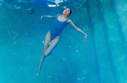 Image of an adult swimmer floating calmly in clear water — expression relaxed, bubbles rising, sunlight streaming through the surface.
